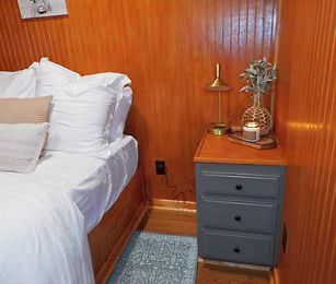 Cozy bedroom corner with a white bed, wood-paneled wall, and small gray nightstand with decor