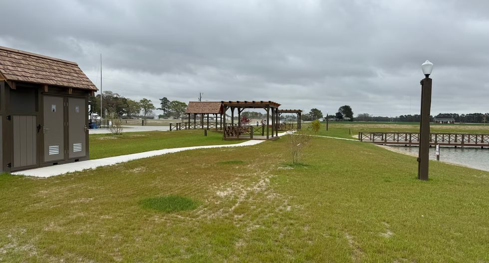 Grassy park with pergola, paved paths, and wooden posts under a cloudy sky