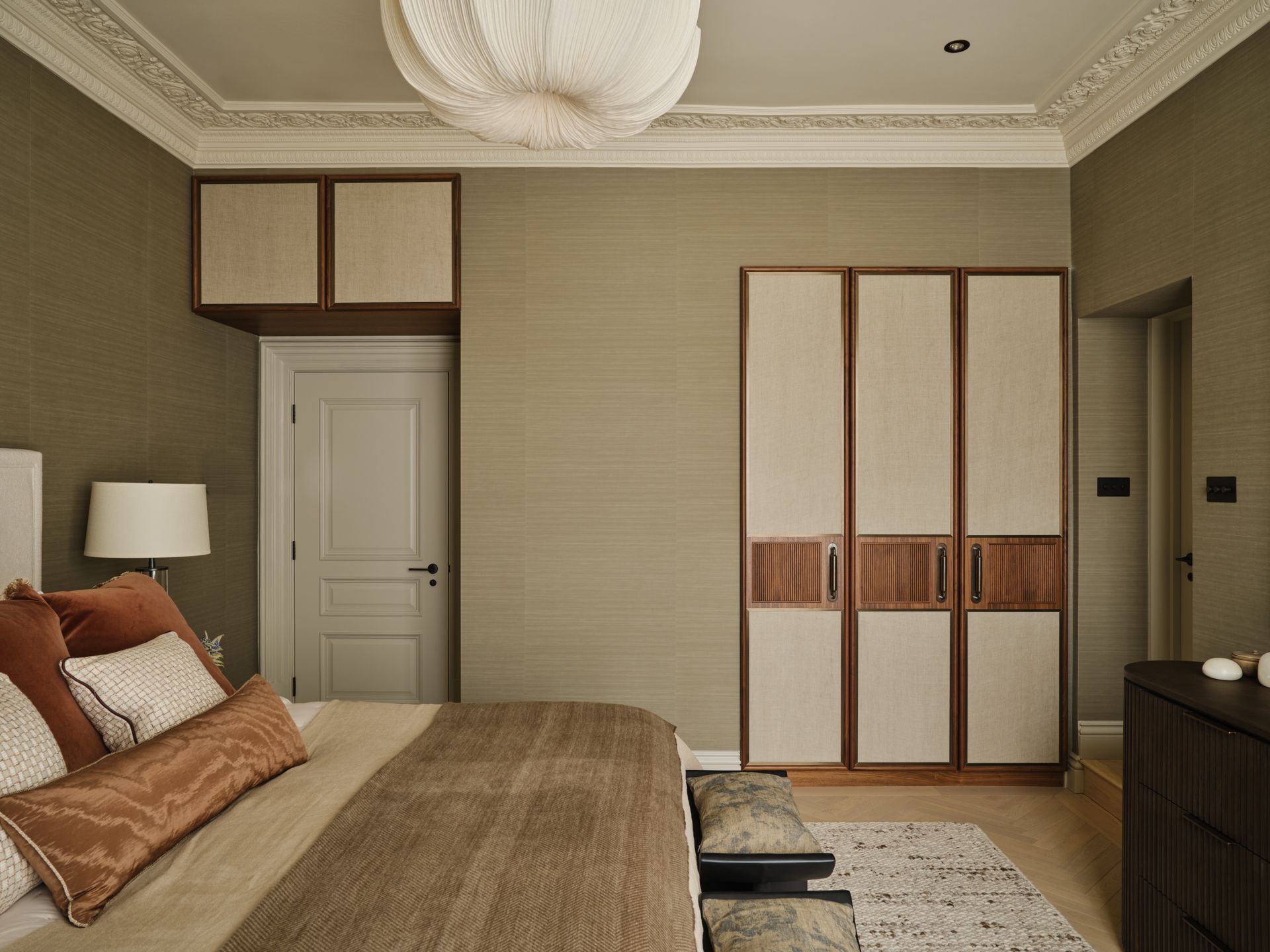 Modern bedroom with beige walls, a bed, wardrobe, dresser, and white door.