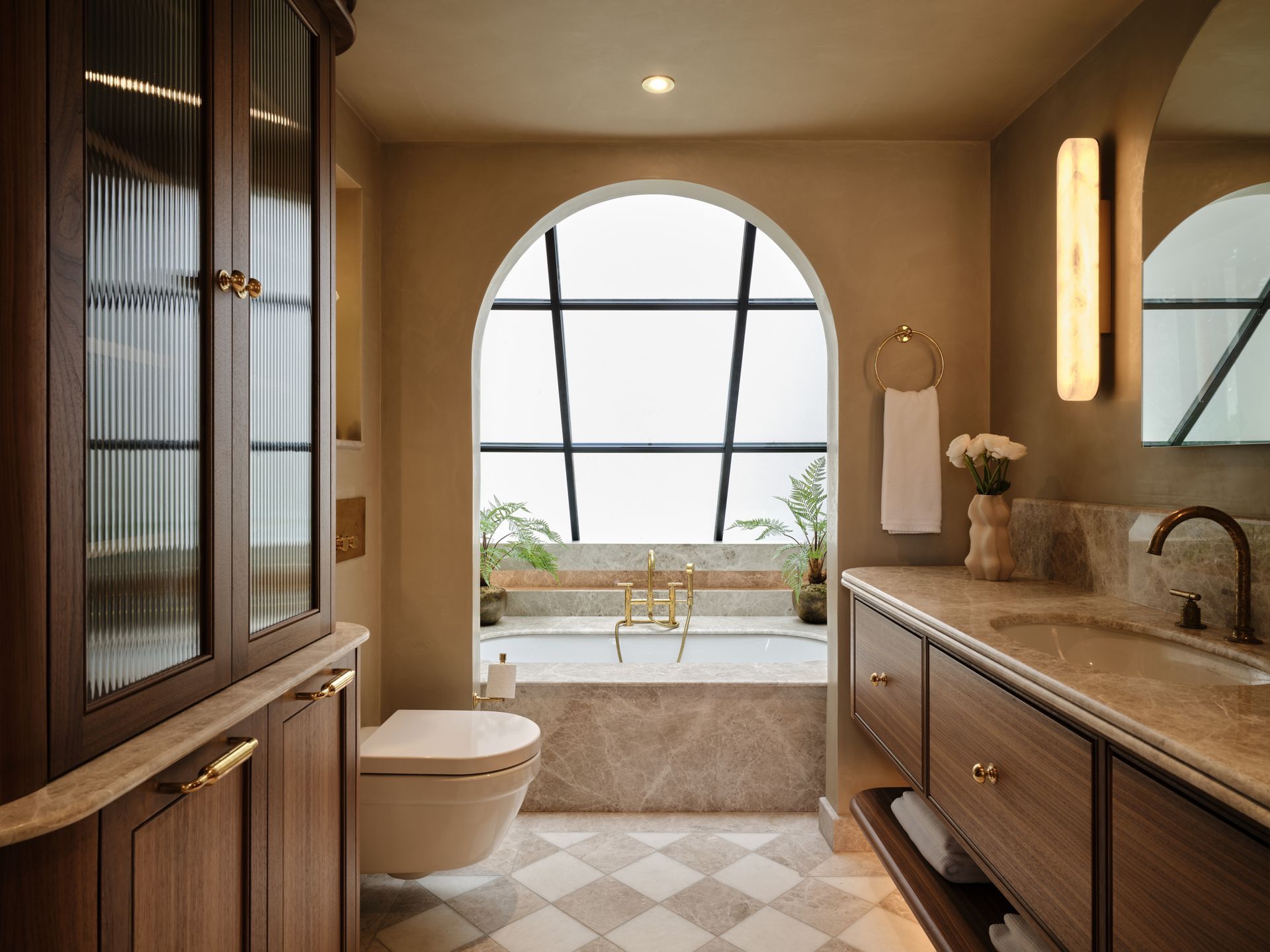 Elegant beige bathroom with arched window, soaking tub, wood vanity, and large mirror