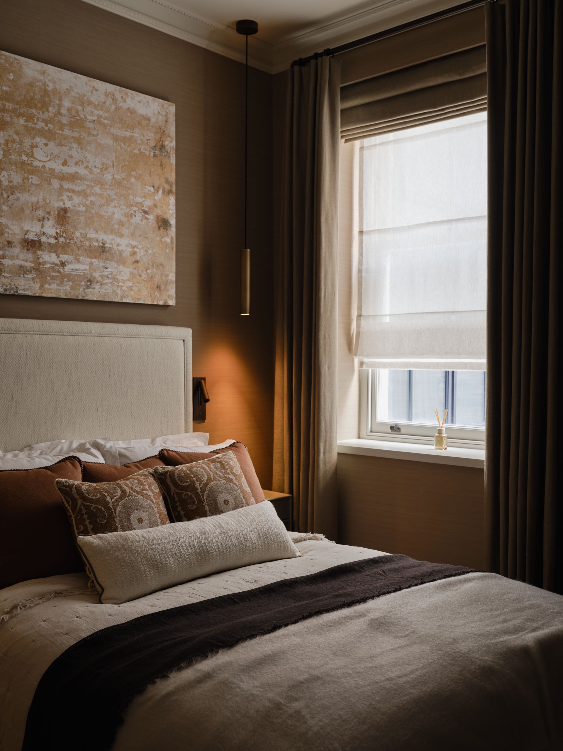 Cozy bedroom with a neatly made bed, warm lighting, and a large window with blinds