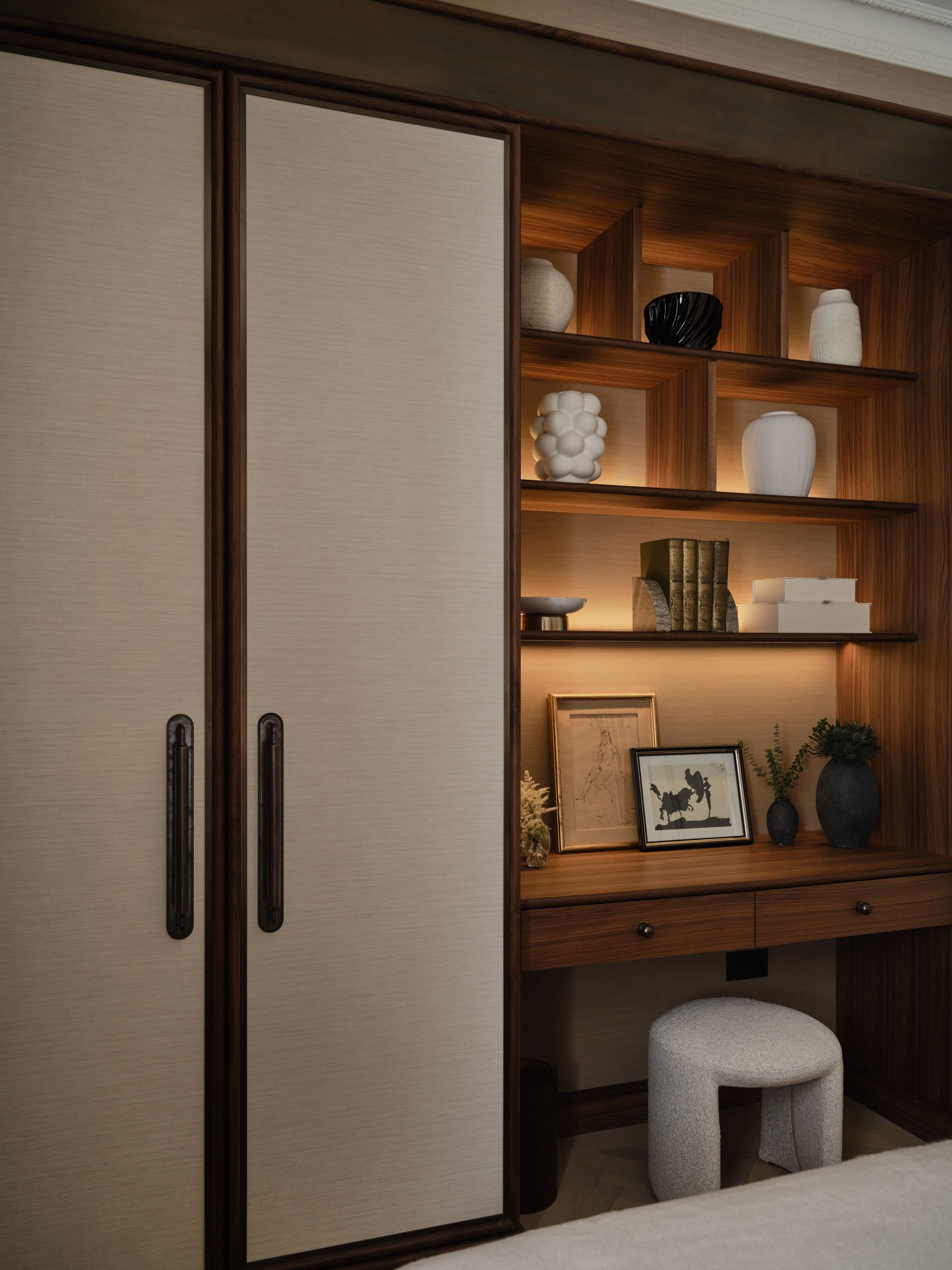 Built-in shelving and wardrobe with books, decor, and a small stool in a cozy room