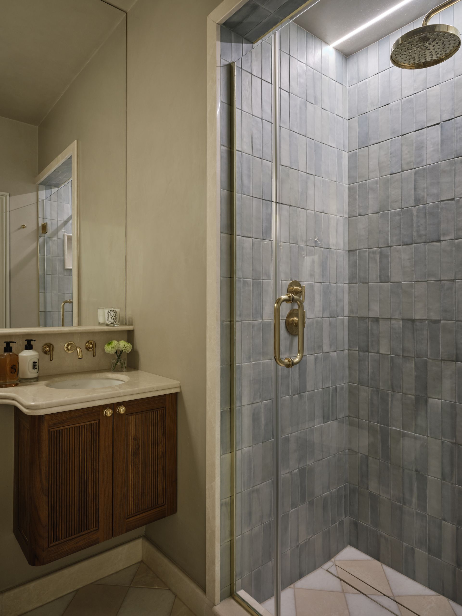 Bathroom vanity beside a glass-enclosed shower with gray tile and brass fixtures