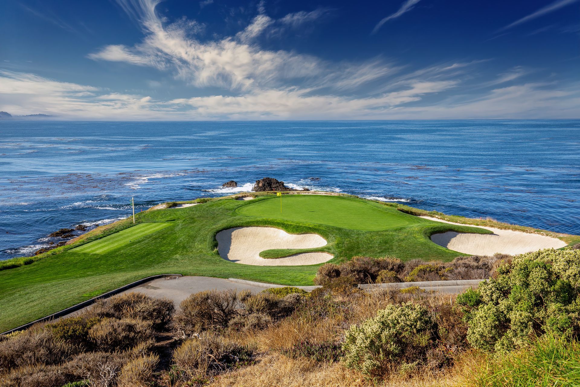 Golf green on a peninsula, overlooking the blue ocean. Sand traps and green grass in bright sunlight.