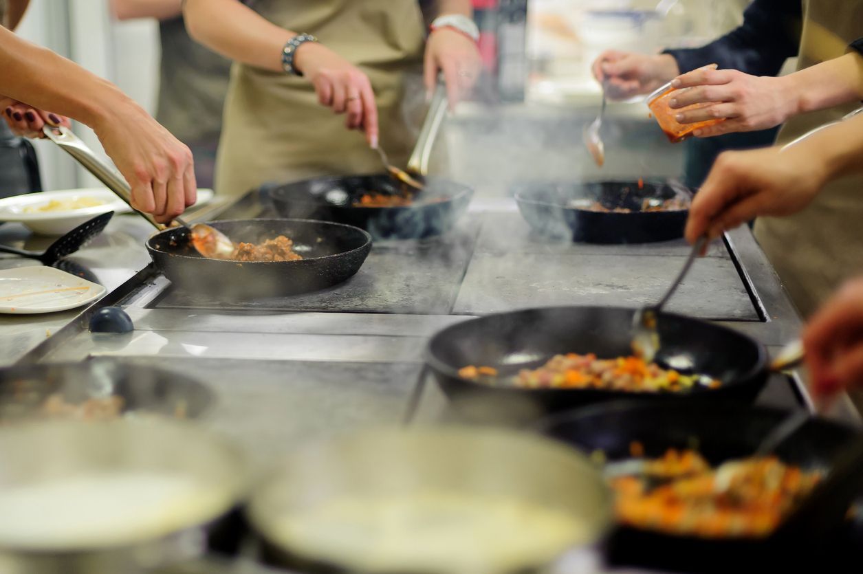 People cooking at stove, cooking class. Pans on stove, steam rising.