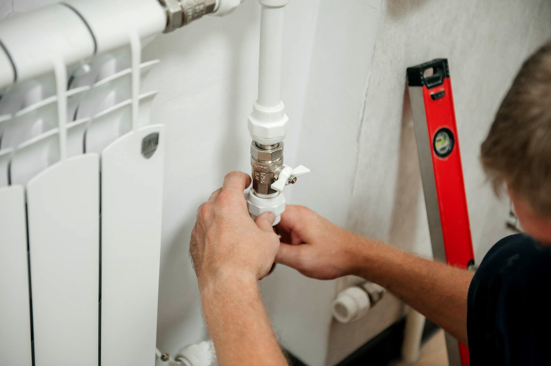 A man is fixing a pipe on a wall next to a red level.