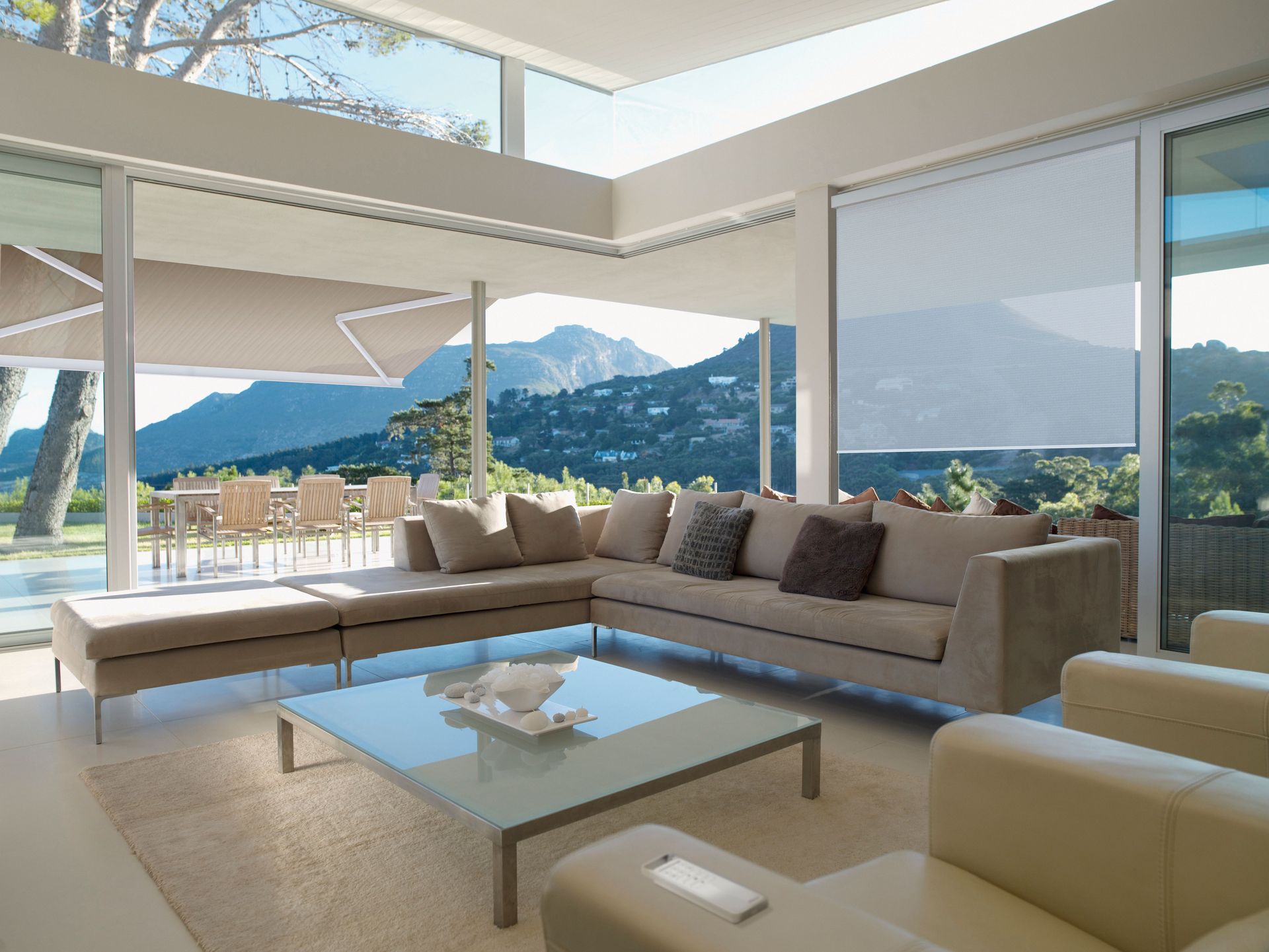 Modern living room with large windows, beige sectional, glass coffee table, and mountain view