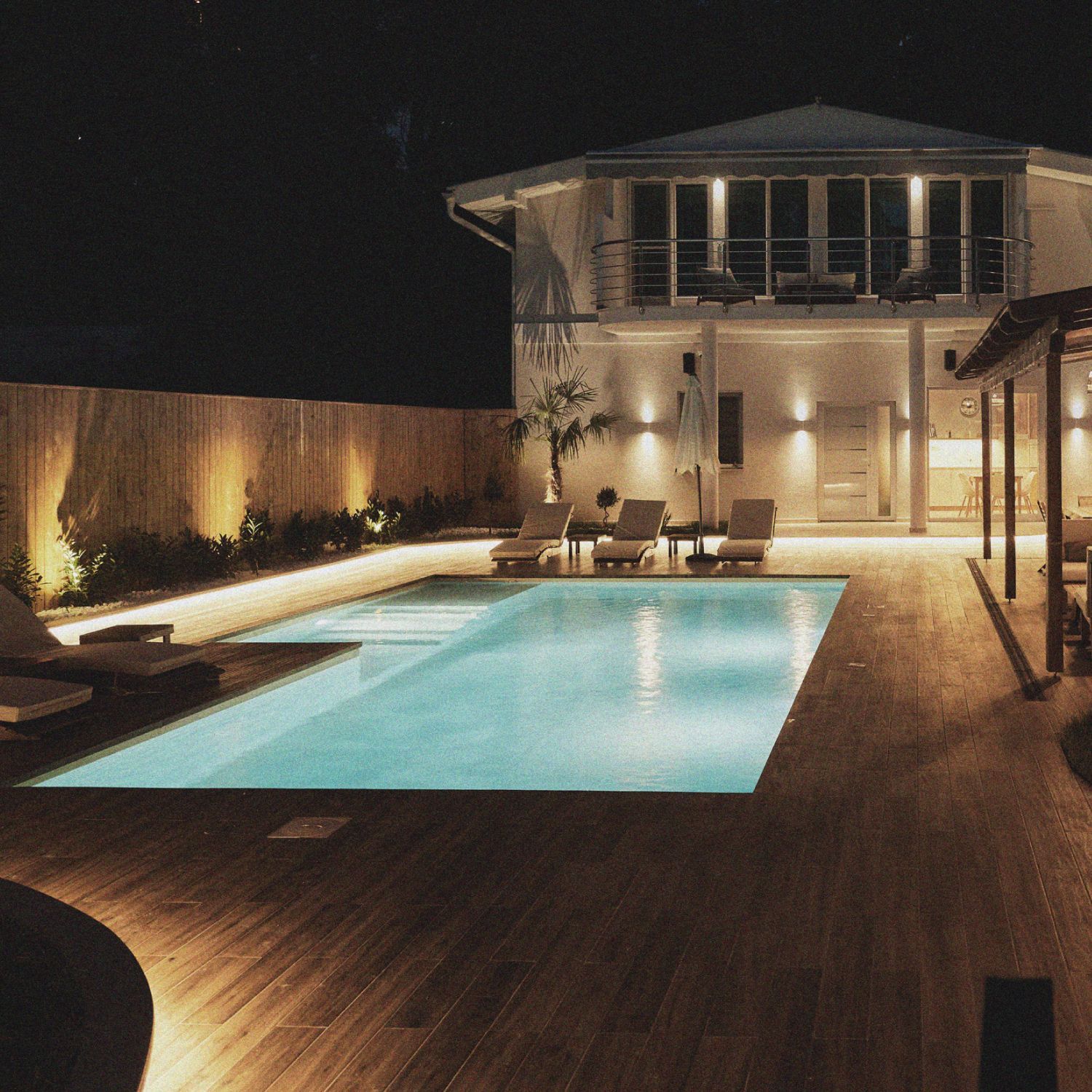 Nighttime poolside patio with glowing lights and a modern two-story house