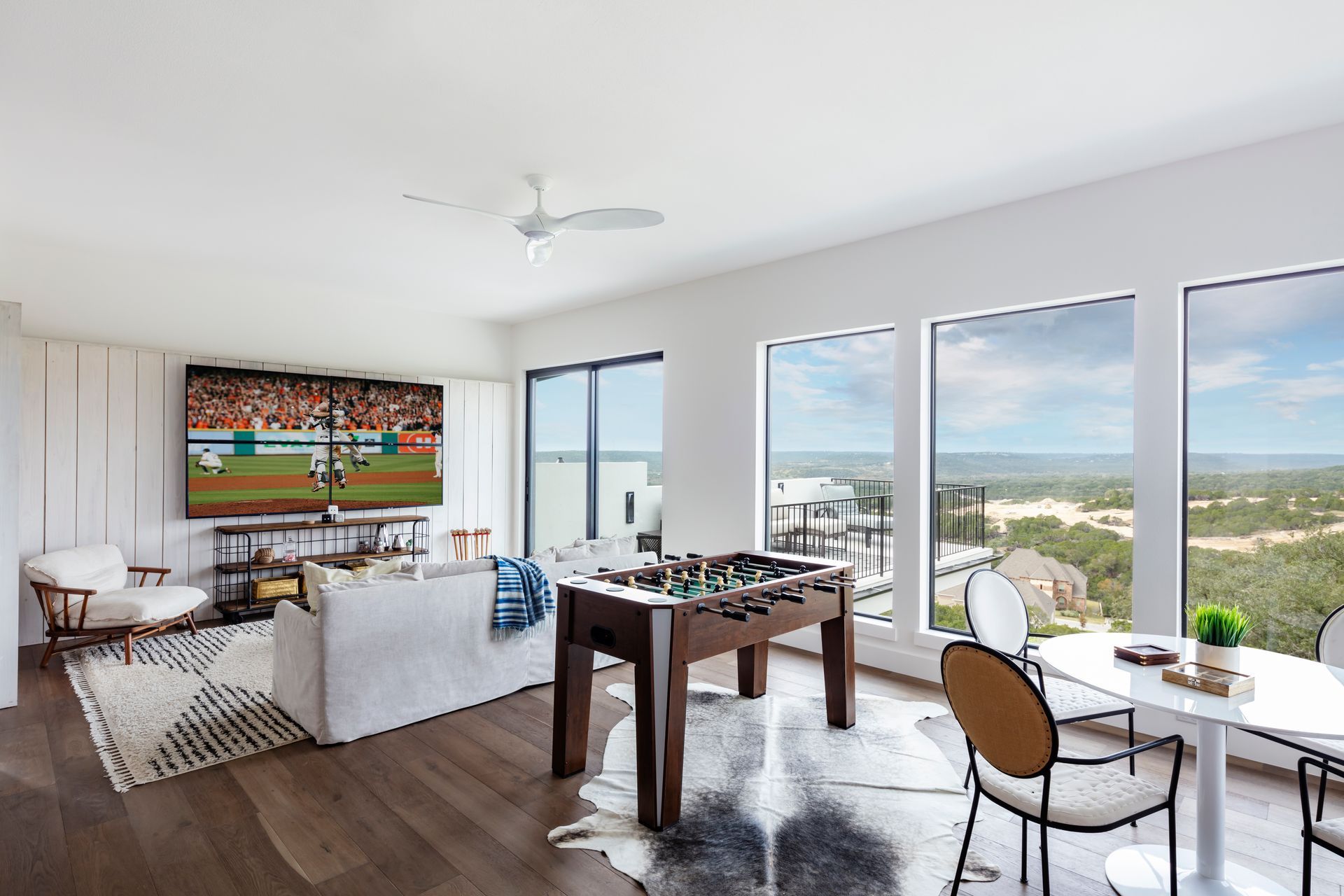 Bright living room with large windows, white sofa, TV, dining table, and city/ocean view