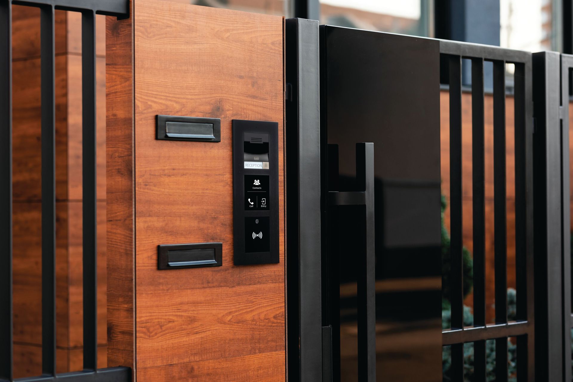 Modern black metal gate with wood panel and keypad intercom at an entrance