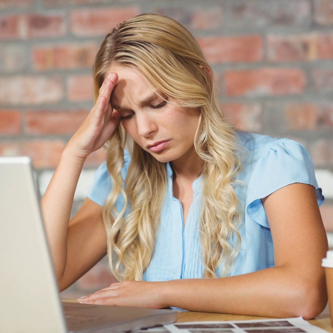 A Woman Sits With Her Hand On Her Forehead — Michelle Crutcher Business Coaching & Consulting in The Entrance North, NSW