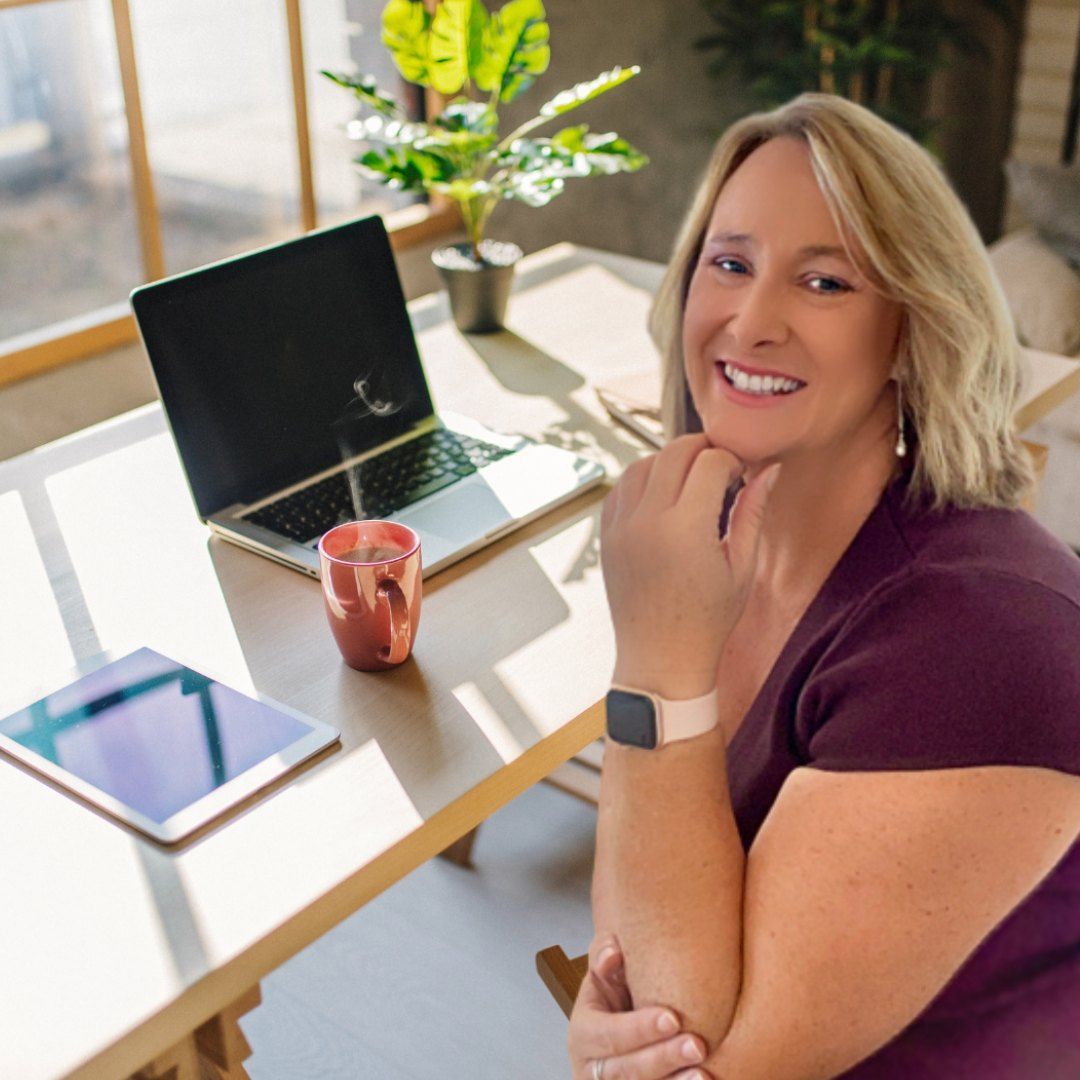 A Smiling Woman Sits At A Table With A Laptop — Michelle Crutcher Business Coaching & Consulting in The Entrance North, NSW
