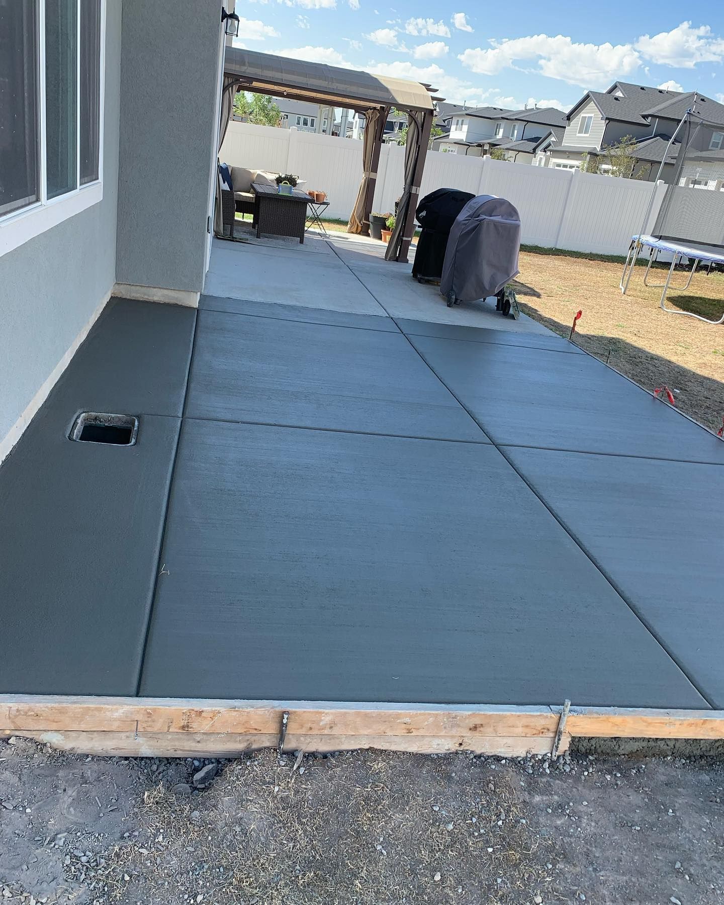 A concrete patio is being built in the backyard of a house.