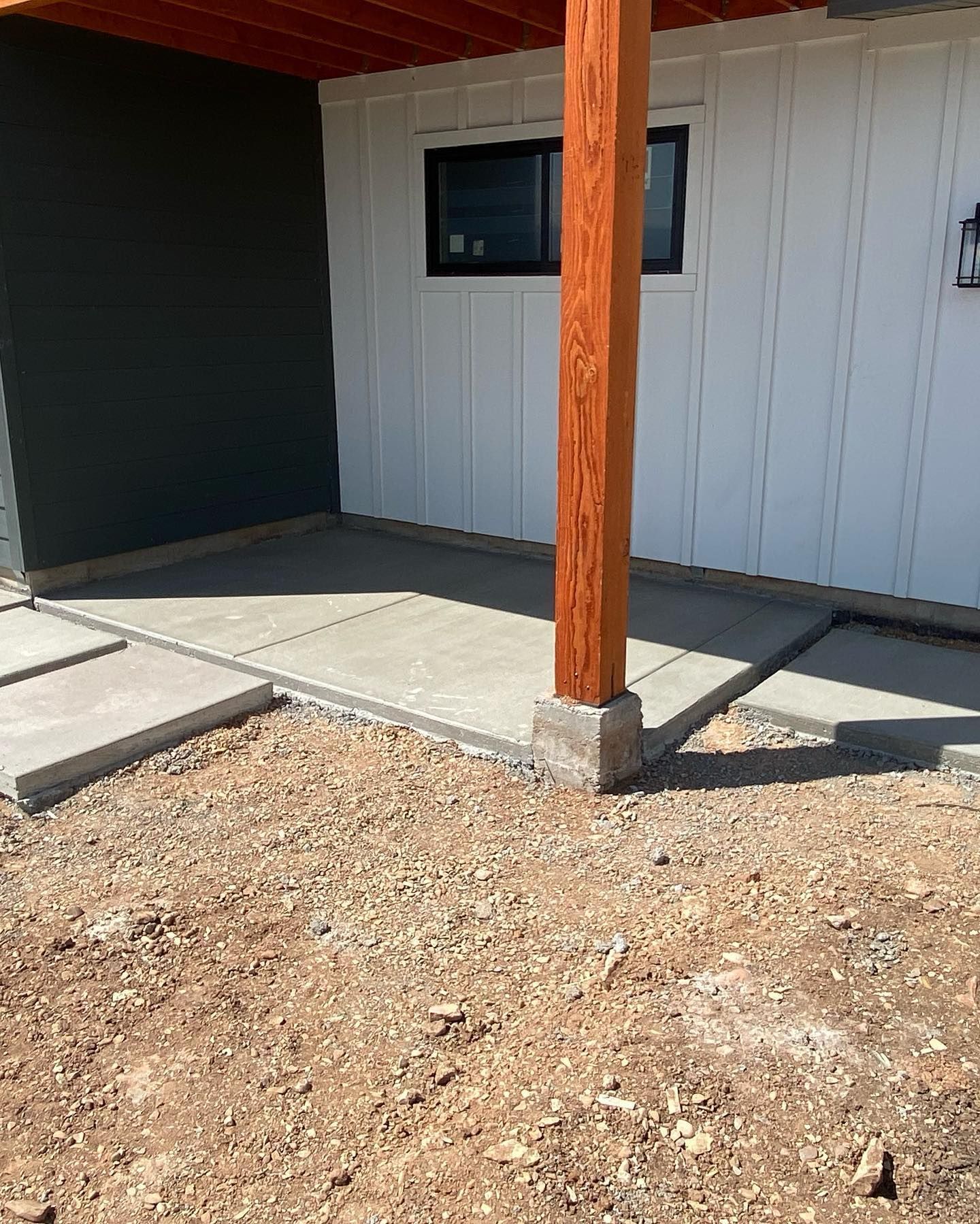 A concrete walkway with a wooden post in front of a house.