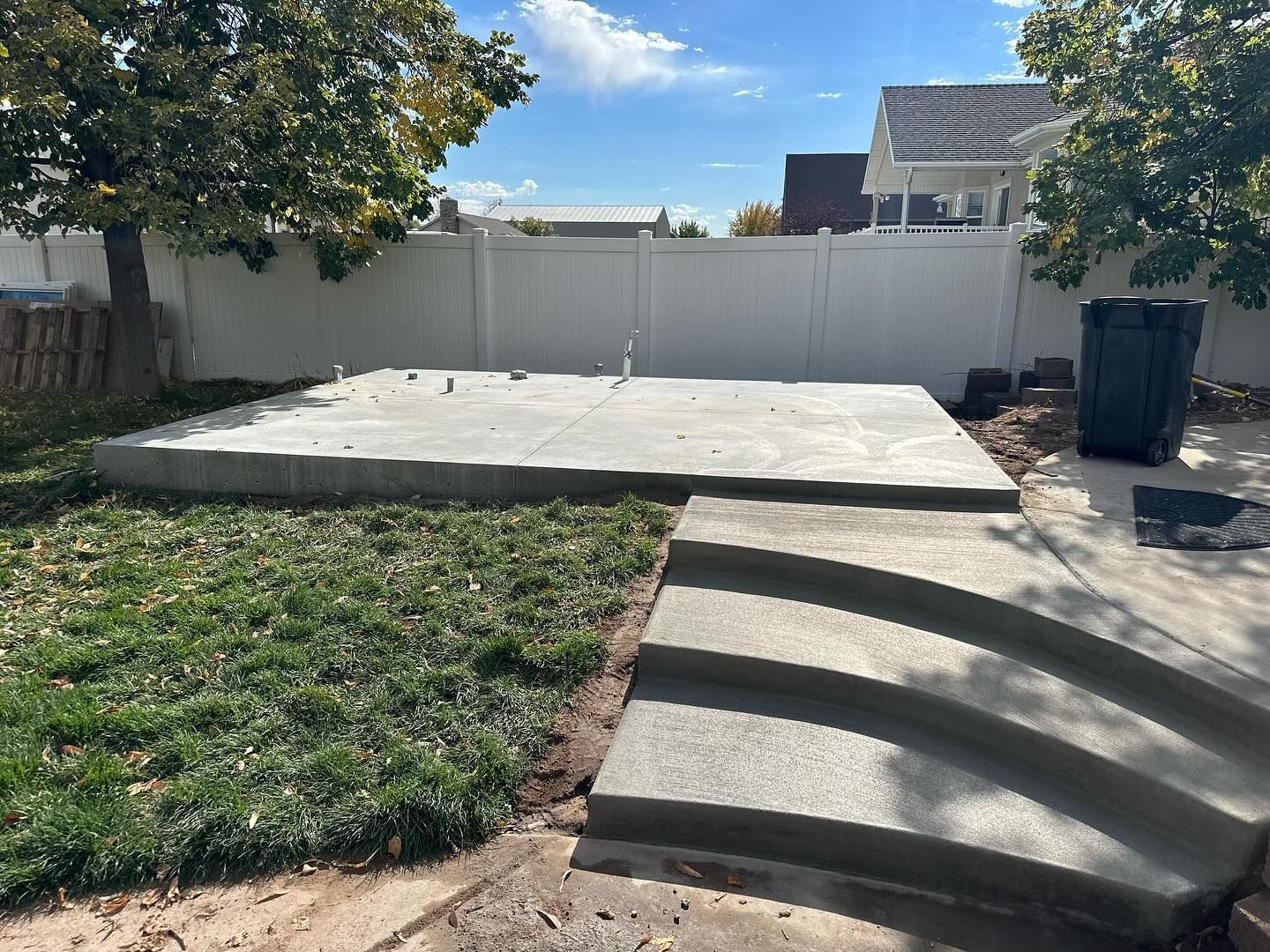 A concrete patio with stairs and a white fence in the backyard.