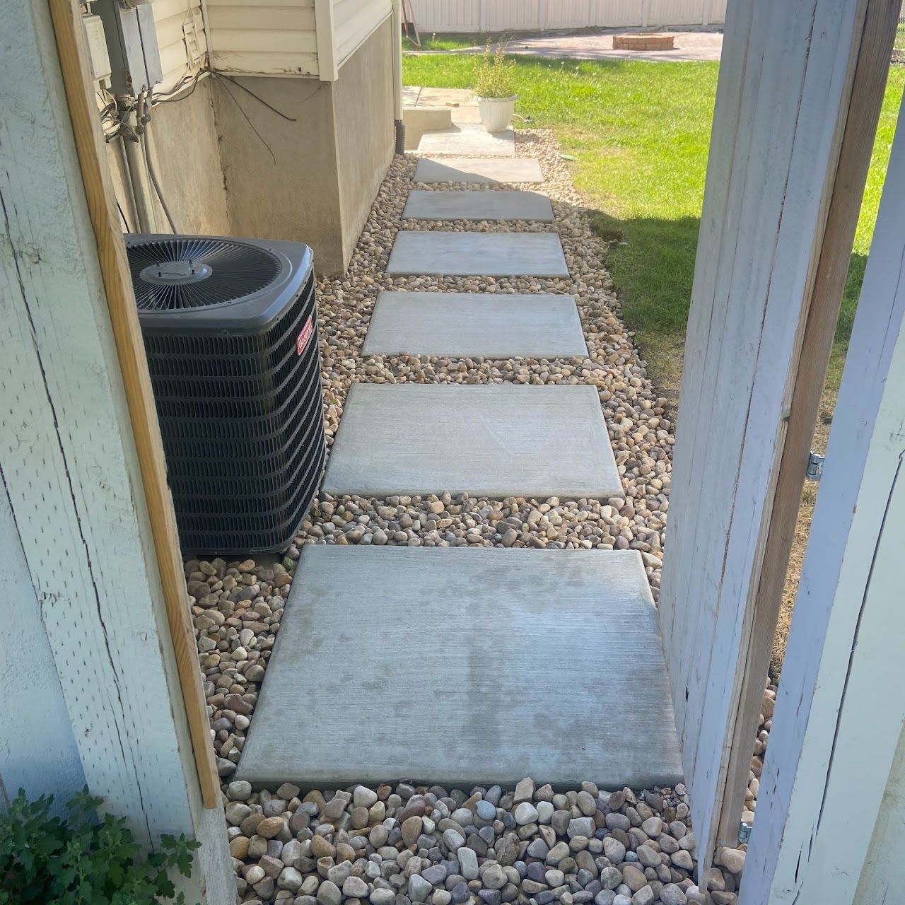 A walkway leading to a house with a black air conditioner