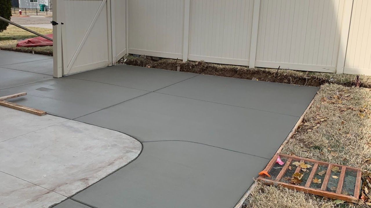 A concrete driveway is being built next to a white fence.