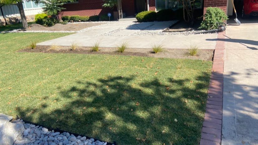 A person is standing in front of a brick house with a lush green lawn.