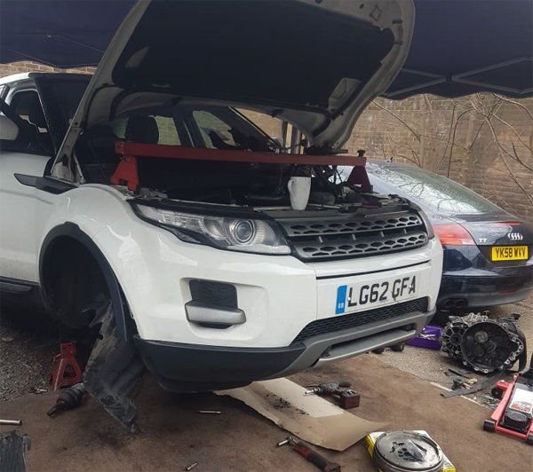 Picture of a white car with its bonnet open while it is being fixed