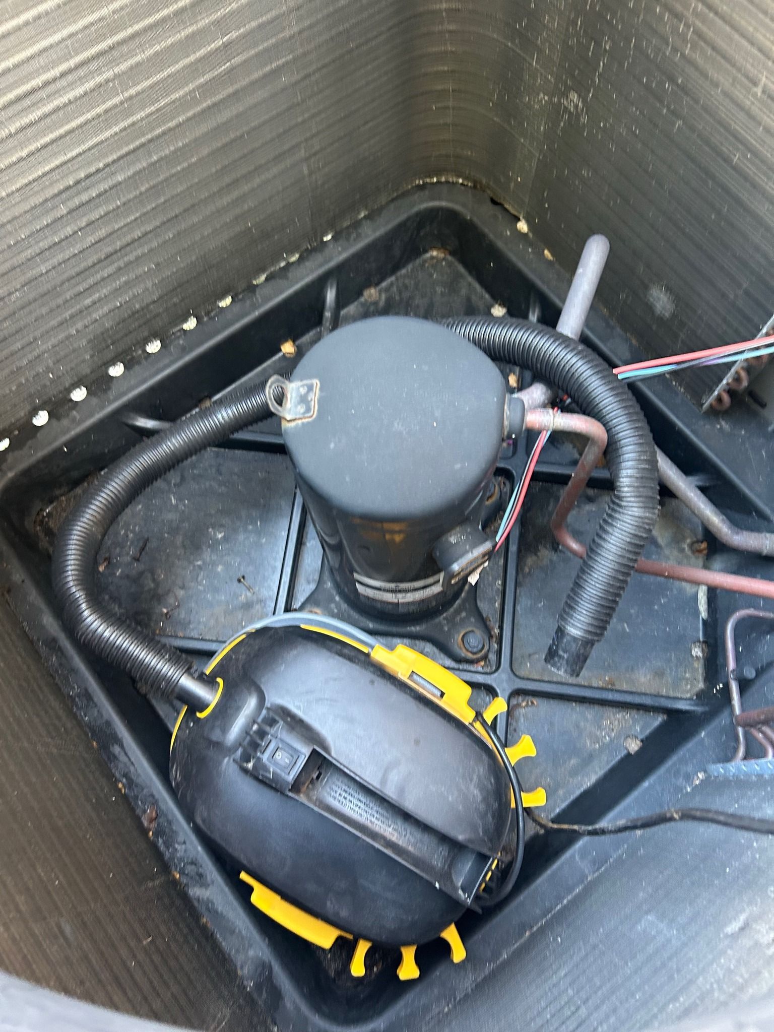An air conditioning compressor inside the outdoor unit. Black and copper components.