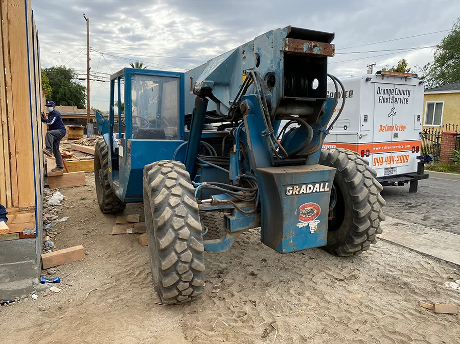 A blue tractor is parked on the side of the road next to a white van.