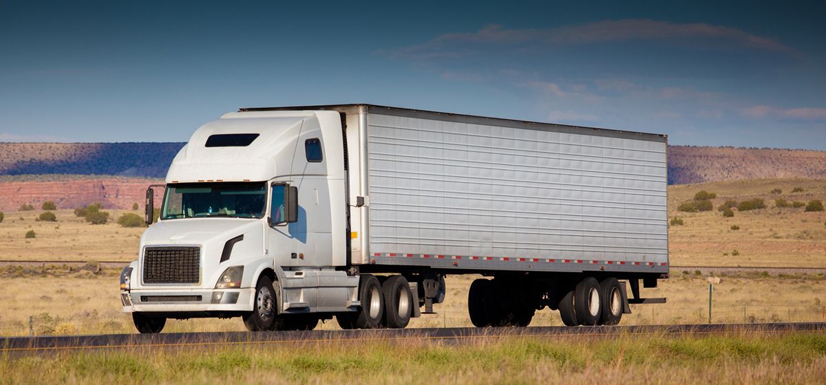 A semi truck is driving down a road in the desert.