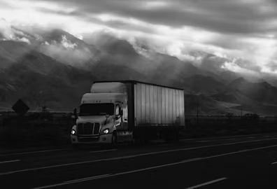 Semi-truck driving on a wet highway with mountains and low clouds in the background