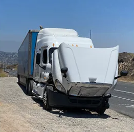 White semi-truck parked on a roadside shoulder with its front hood open, under a clear blue sky
