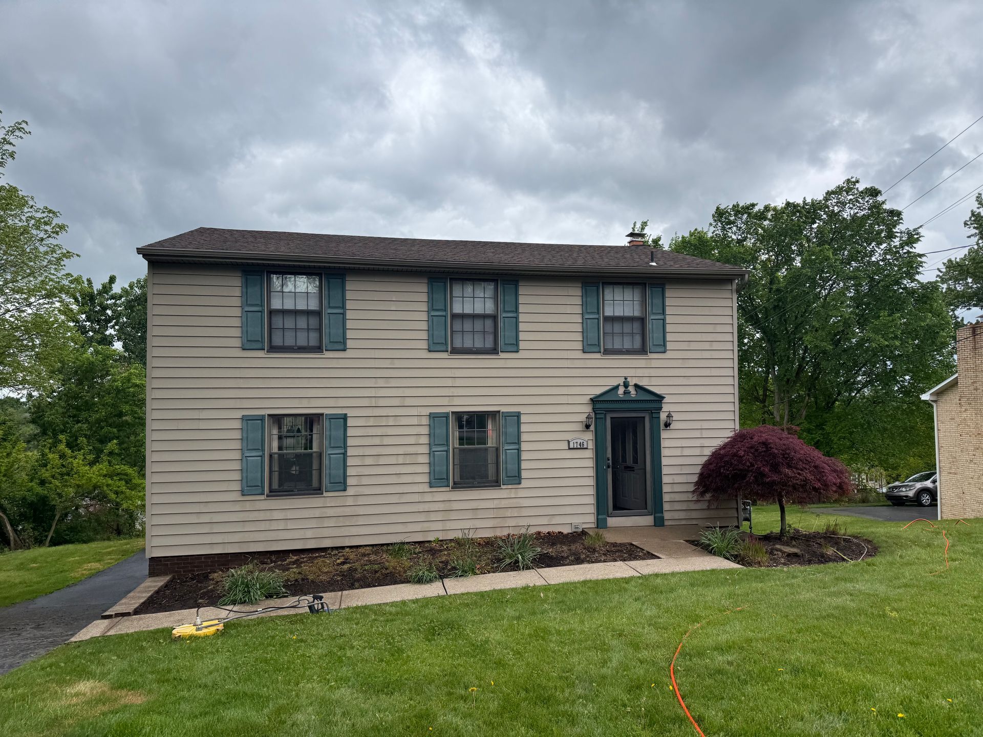 Two-story beige house with green shutters on a wet driveway after being pressure washed