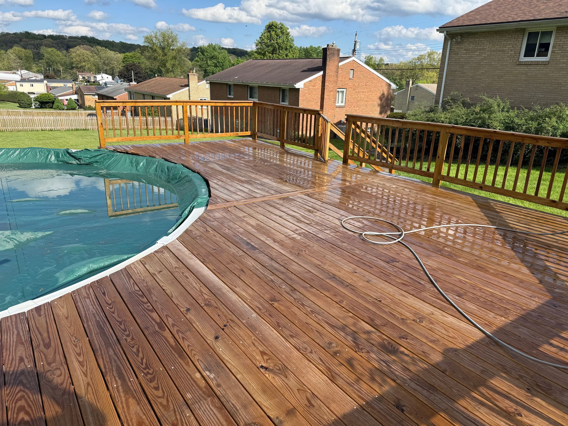 Curved wooden pool deck with railing beside a backyard swimming pool on a sunny day