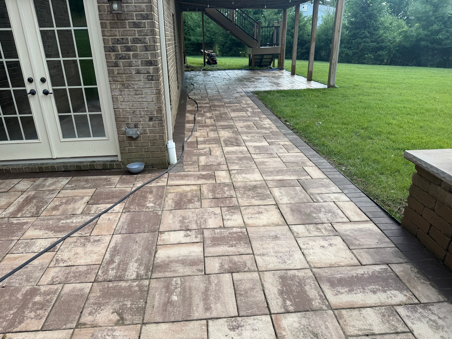 Stone patio beside a brick house, with white French doors and a green lawn in the backyard.