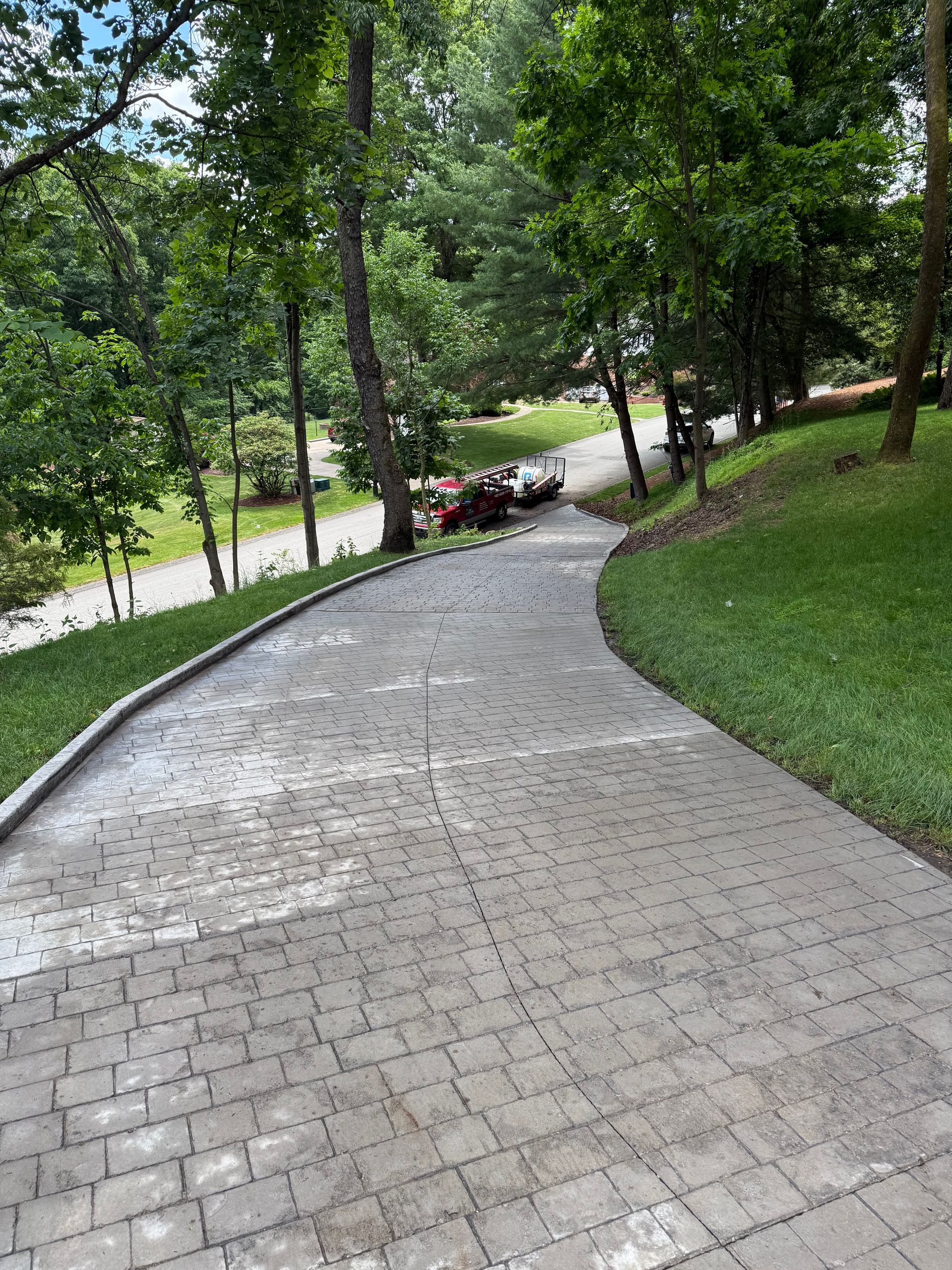 Curved brick path through a green park with trees and a road in the distance