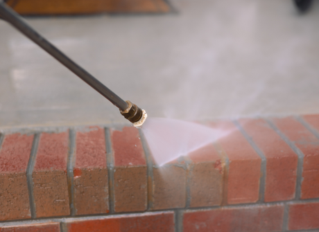 Pressure washer spraying water onto a brick wall outdoors