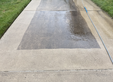 Wet concrete sidewalk patch with darker repaired section down the center