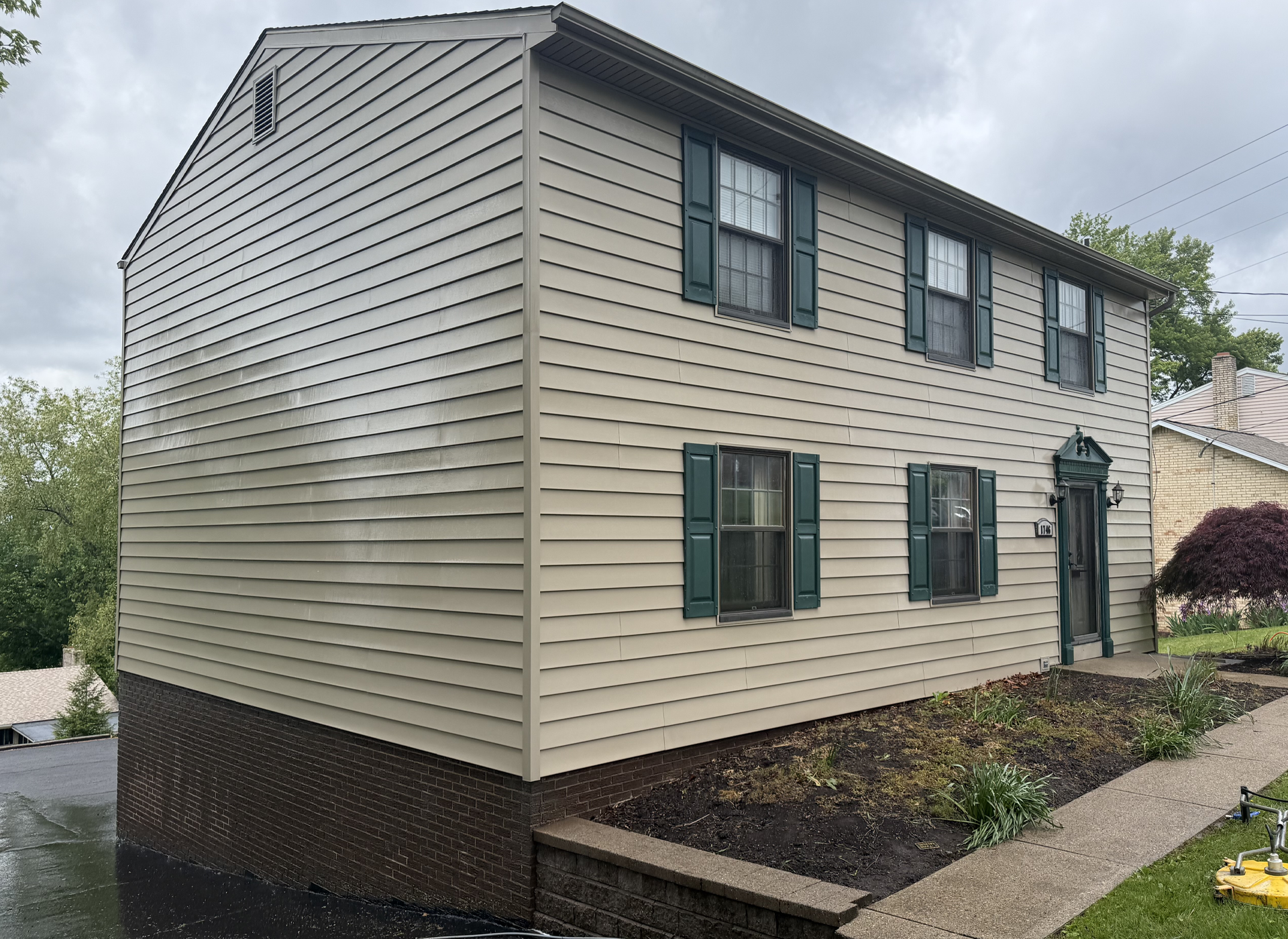 Two-story beige siding house with green shutters on a wet driveway after being pressure washed or 