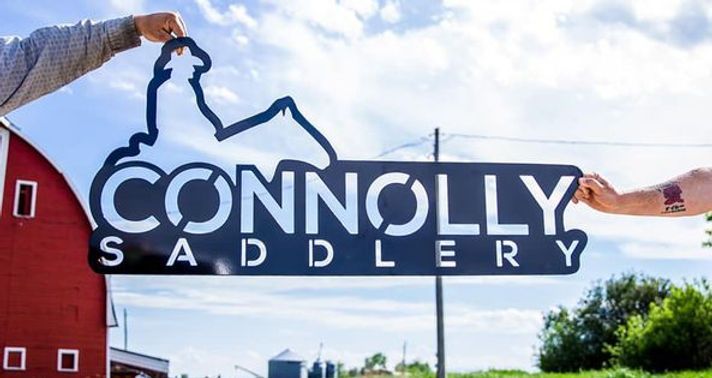two people are holding a sign that says connolly saddlery in front of a red barn .