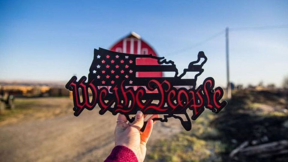a person is holding a sign that says we the people in front of a barn .