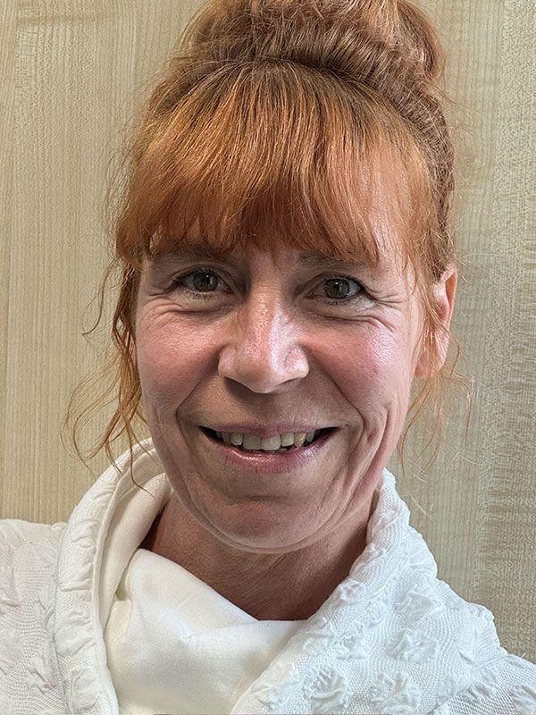 Frau mit rotem Haar zu einem Dutt lächelt und trägt drinnen einen weißen Bademantel.