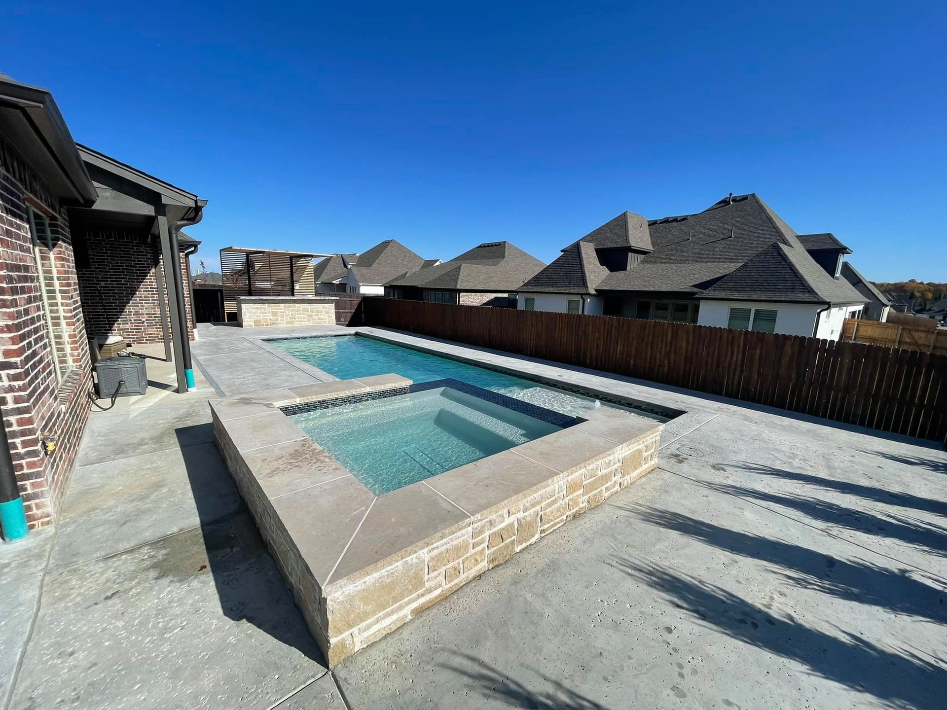 Backyard with a raised rectangular pool and deck beside suburban houses under a blue sky