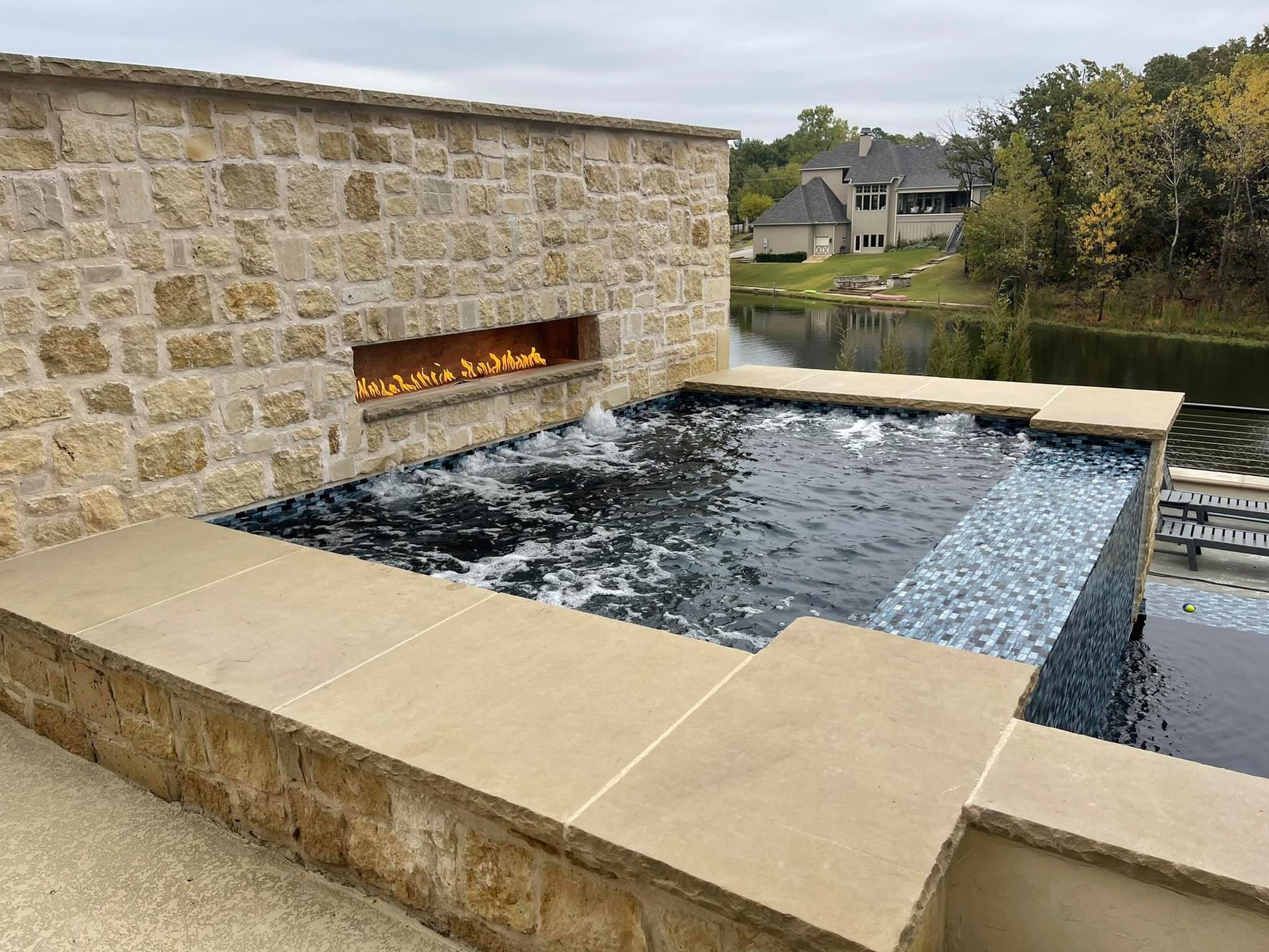 Stone backyard pool with a built-in fire feature and water spilling over the edge