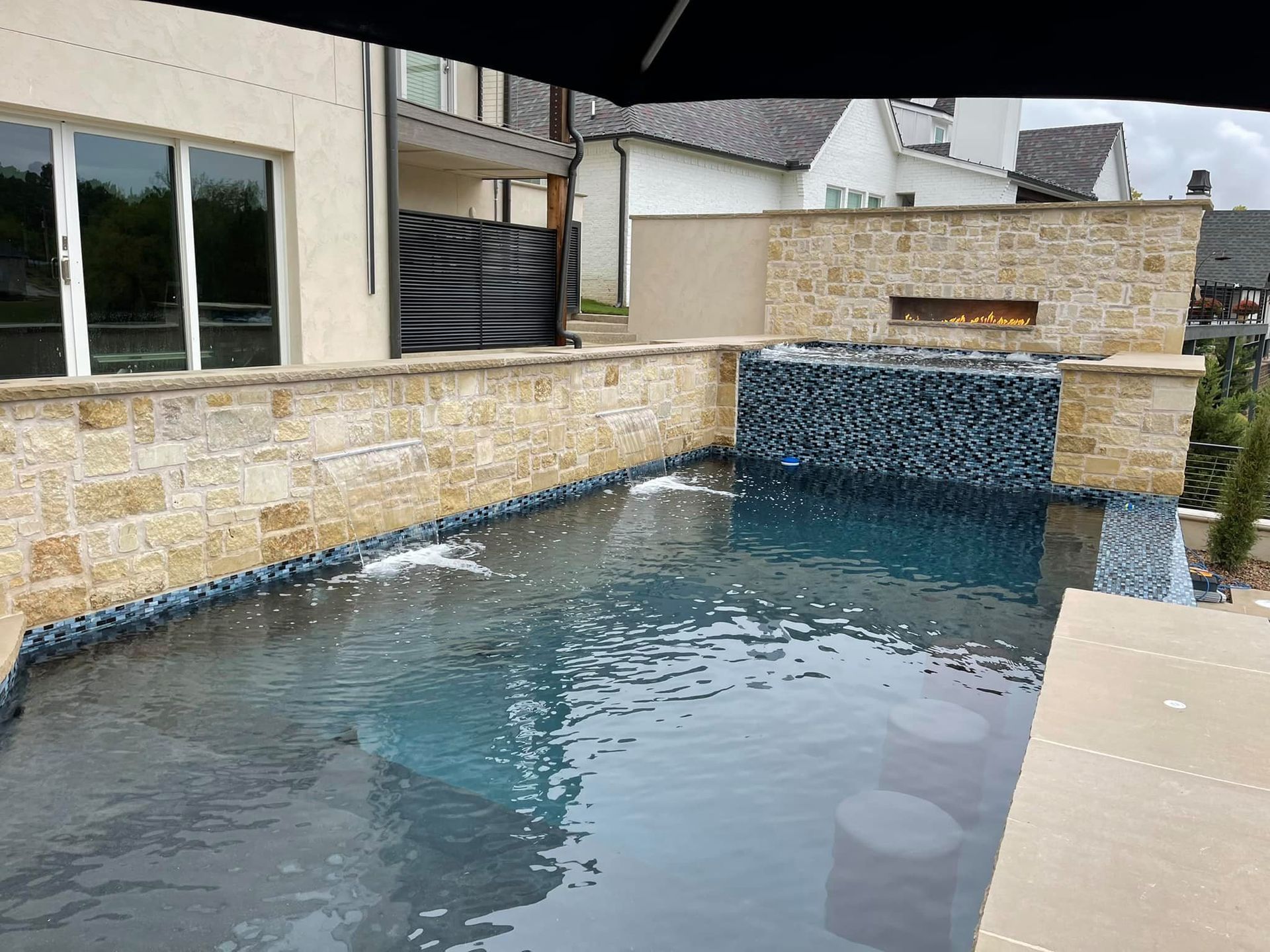 Backyard swimming pool with a stone wall and waterfall feature, reflecting the house and patio.