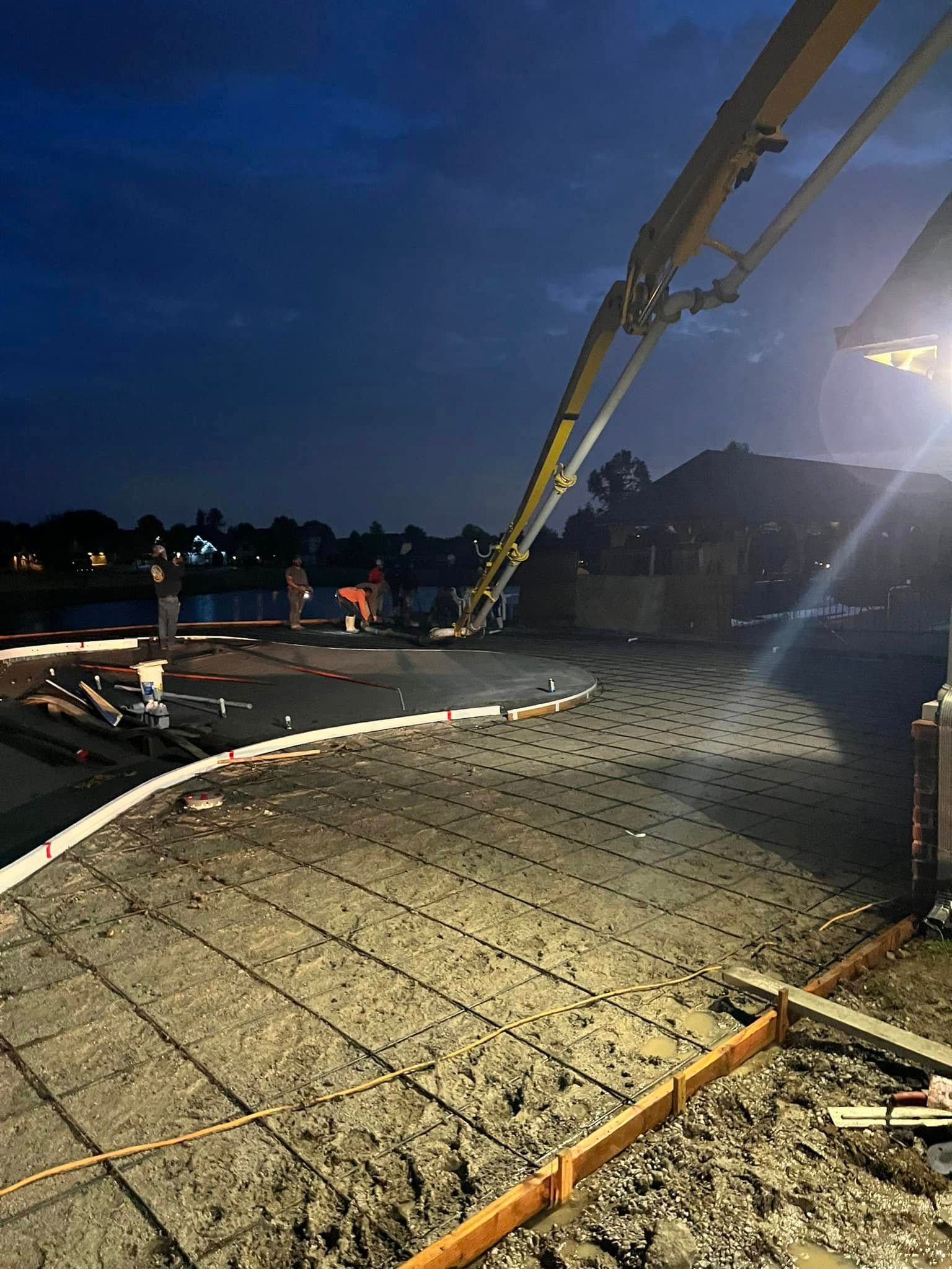 Construction site at dusk with concrete foundation, rebar, and a long boom truck