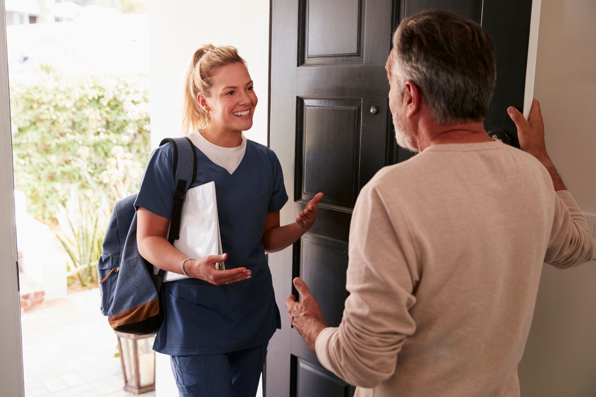 Senior man opening his front door to a female healthcare worker making a home health visit 
