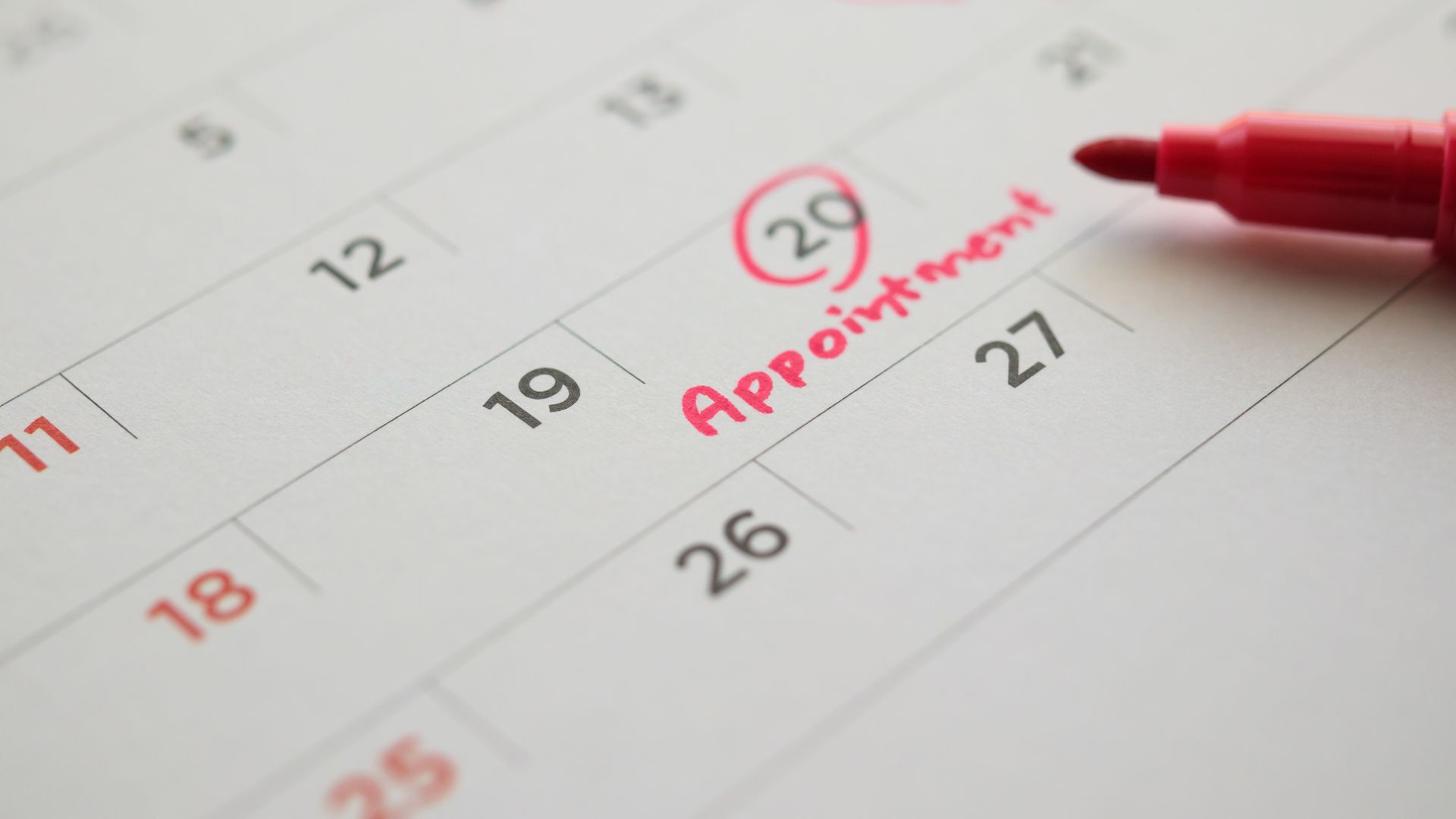 Red color marker pen pointing at important appointment schedule on white calendar page date close up 