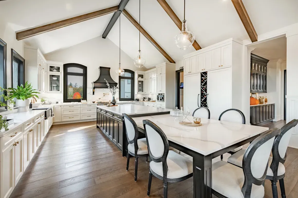 Bright modern kitchen and dining area with vaulted beams, white cabinets, and a long marble table
