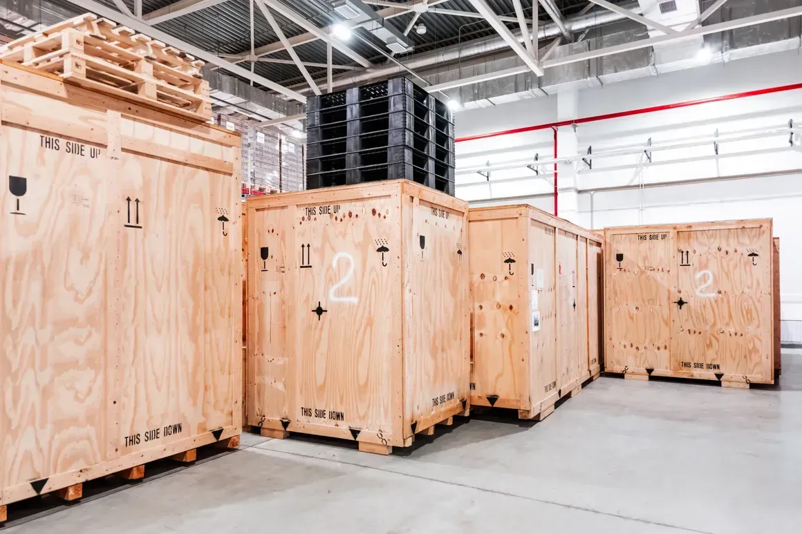 Large wooden storage crates with shipping symbols and markings lined up inside a bright, spacious warehouse.