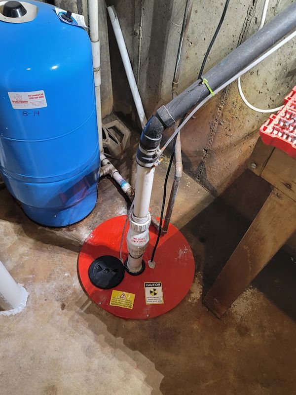 A red radon mitigation system is sitting in a basement next to a blue tank.