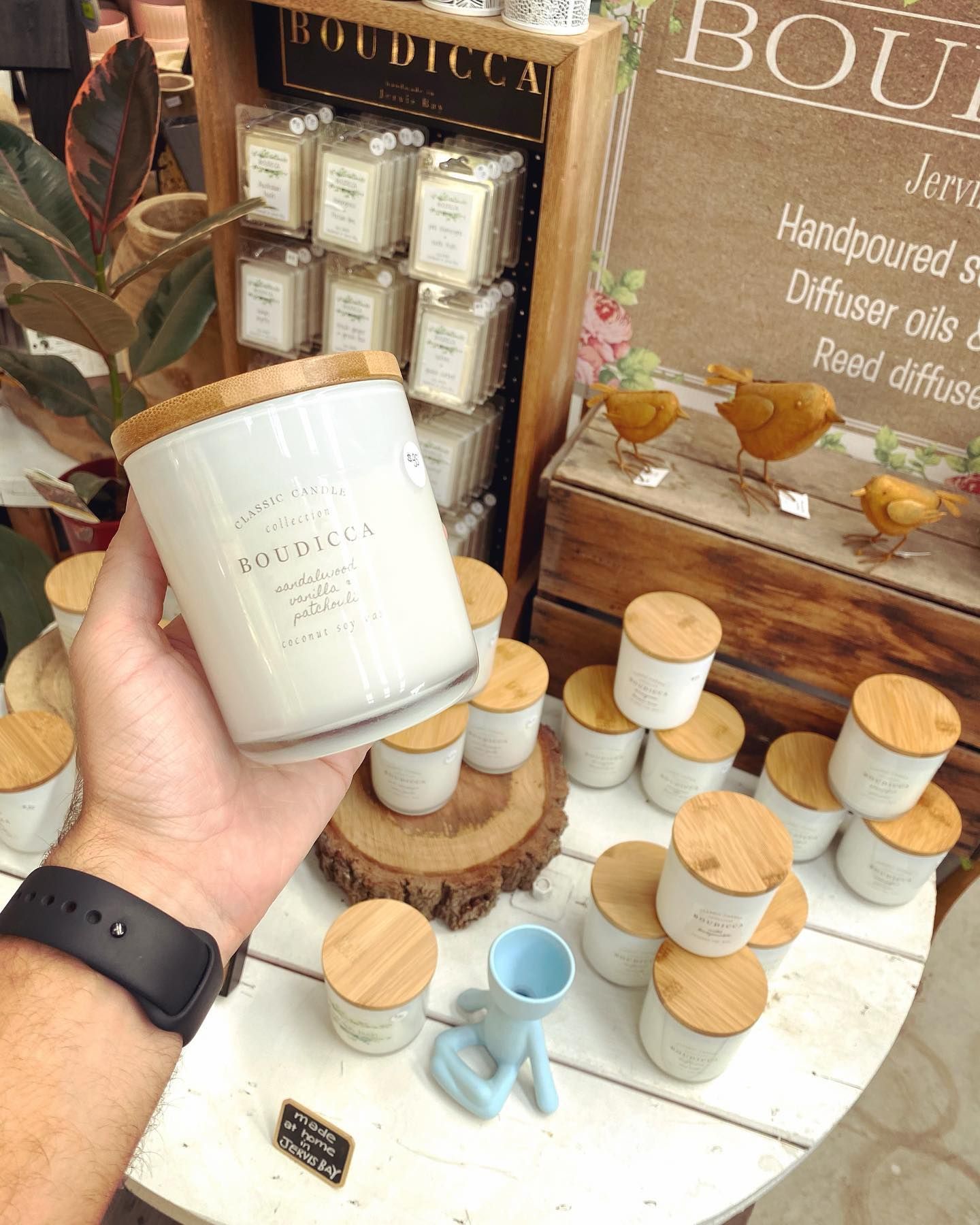 A Person Is Holding A White Candle With A Wooden Lid — Schutz Landscape and Garden Supplies in Tomerong, NSW
