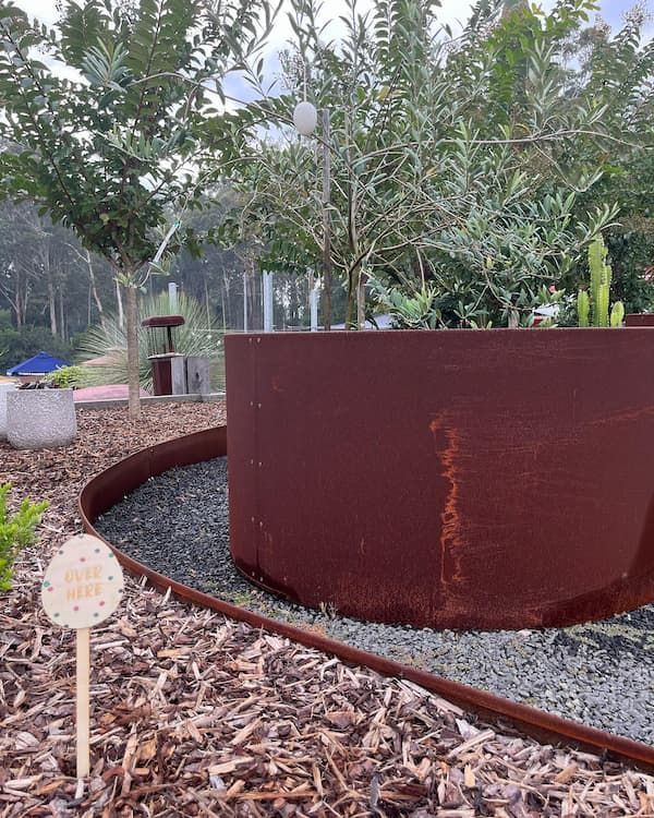 A Rusty Metal Planter In A Garden With Trees In The Background — Schutz Landscape and Garden Supplies in Tomerong, NSW