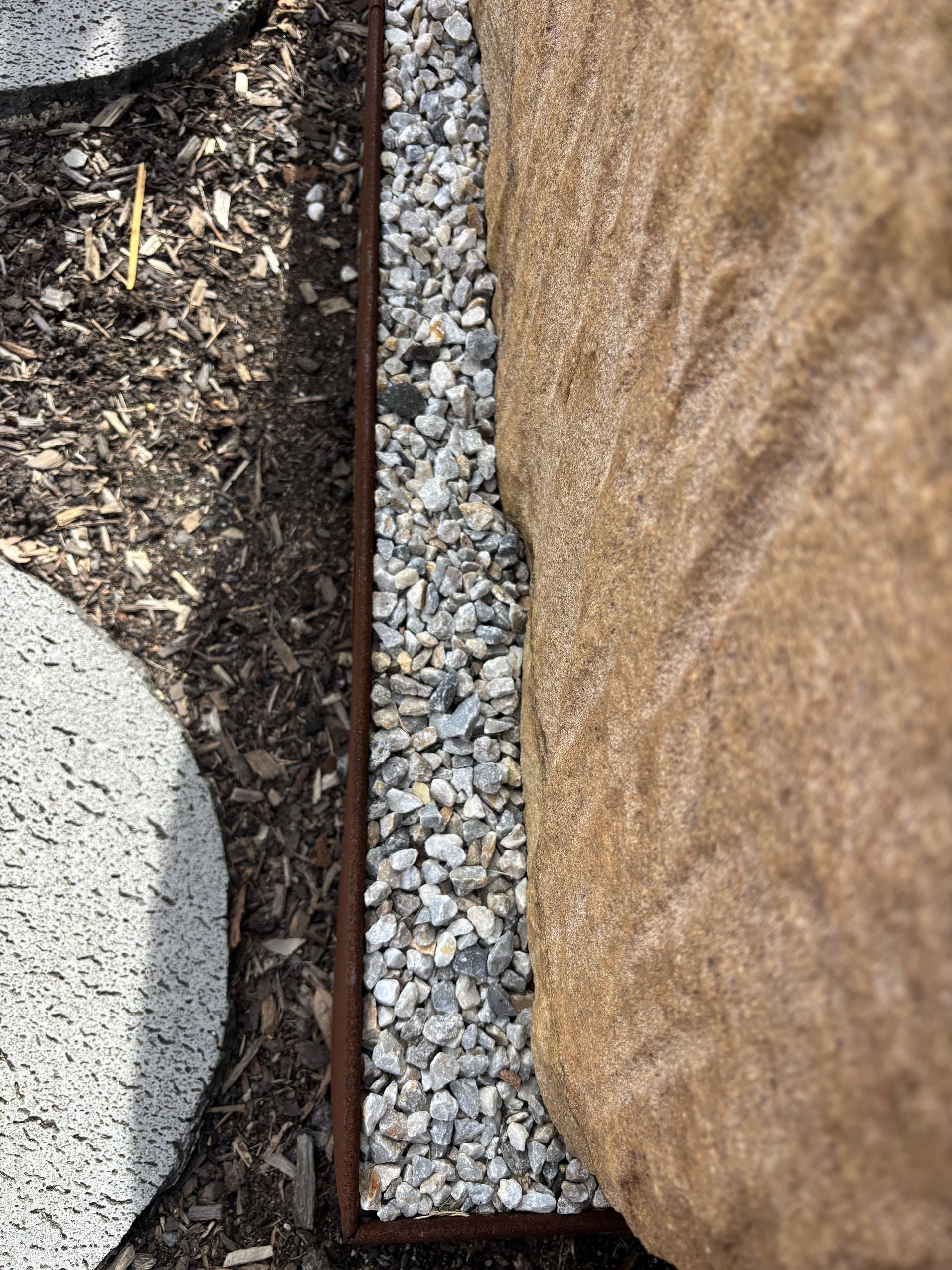 Gravel bed bordered by brown metal, next to a large brown rock and a gray stepping stone, with mulch on left — Schutz Landscape and Garden Supplies in Tomerong, NSW
